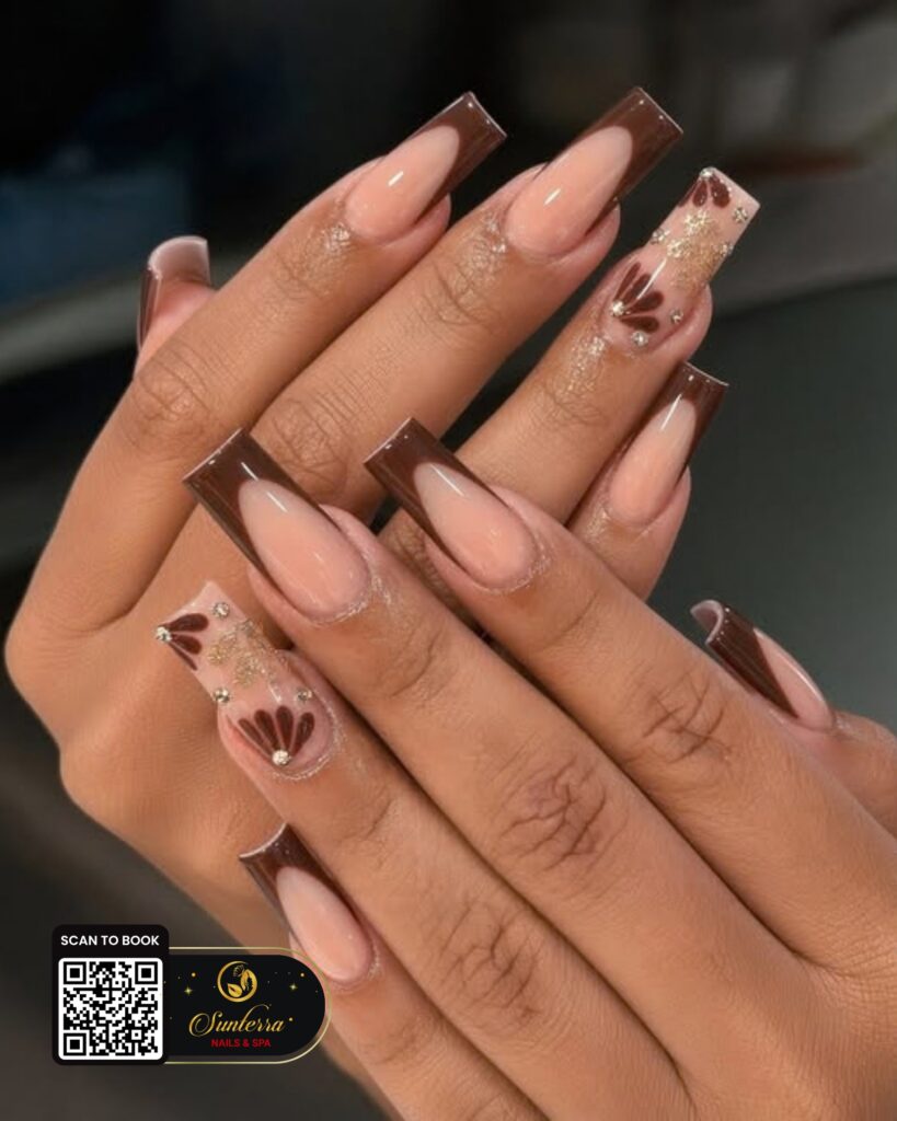 Chocolate French nails with gold flowers shared by Sunterra Nails & Spa on Instagram